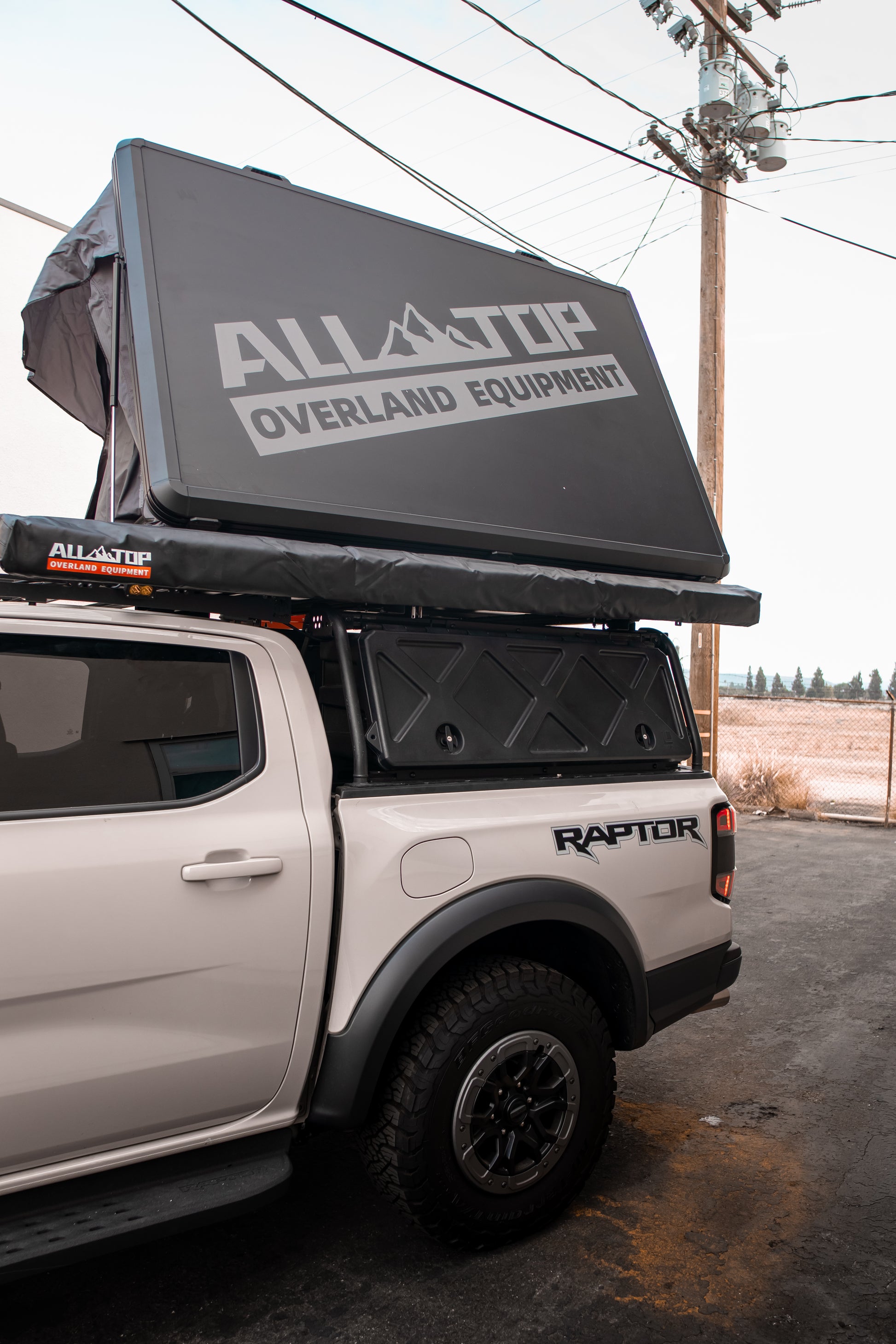White Ford Raptor truck with All Top Overland Equipment roof top tent on a cloudy day.